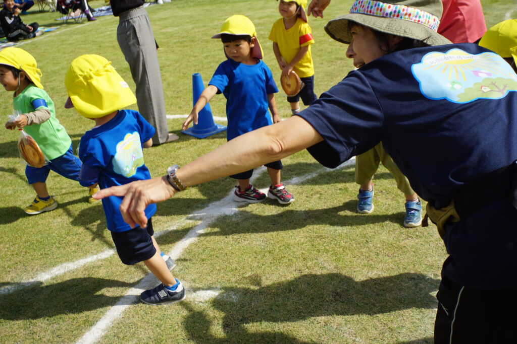 園庭で指を指す先生と幼稚園児たち