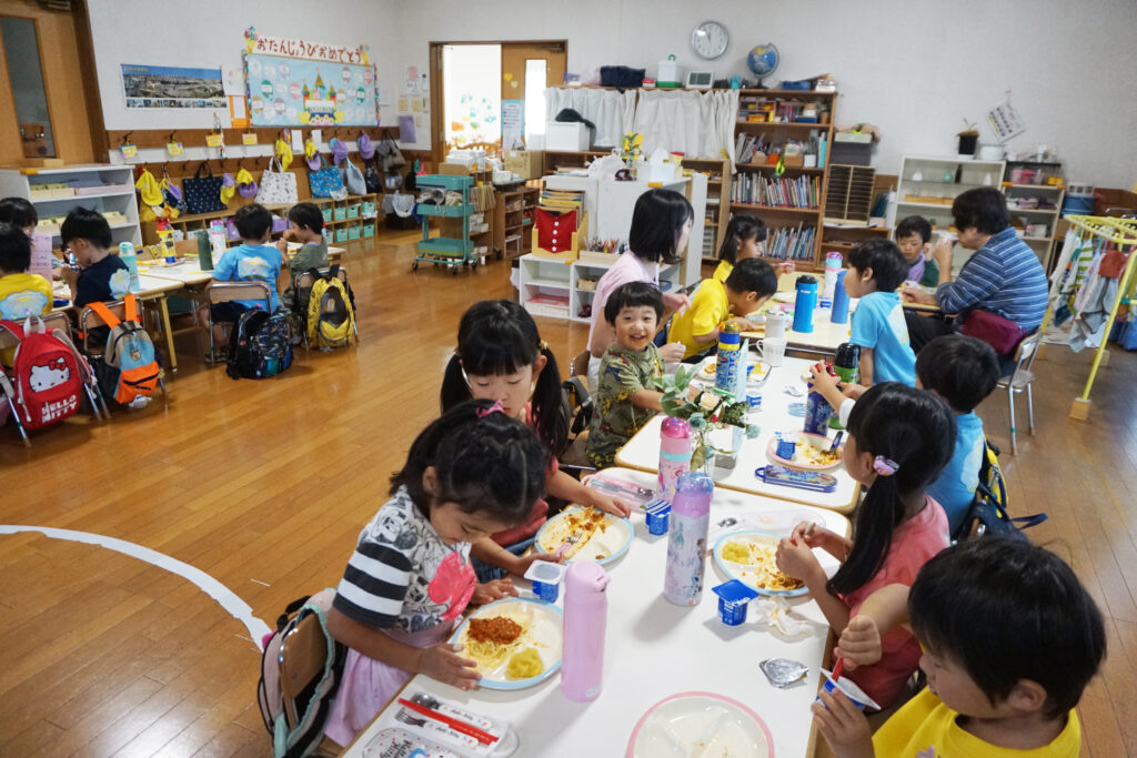 教室で机に座って給食を食べる子供達と先生