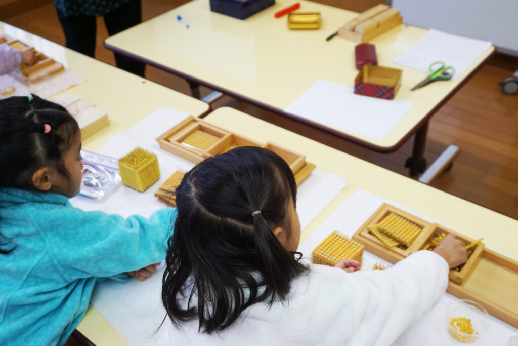 机に向かって金ビーズのお仕事をする幼稚園児たち