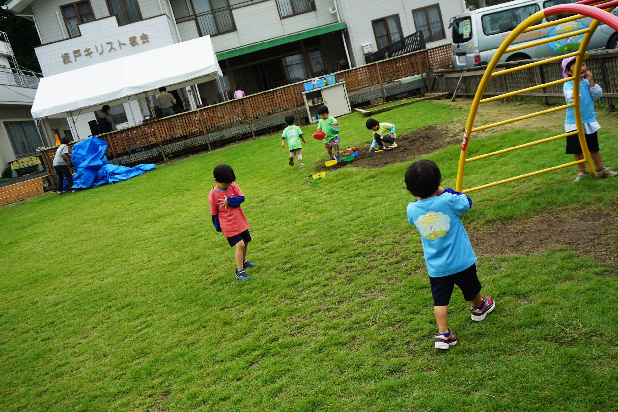 芝生の園庭でかけっこや砂遊びで遊ぶ幼児達